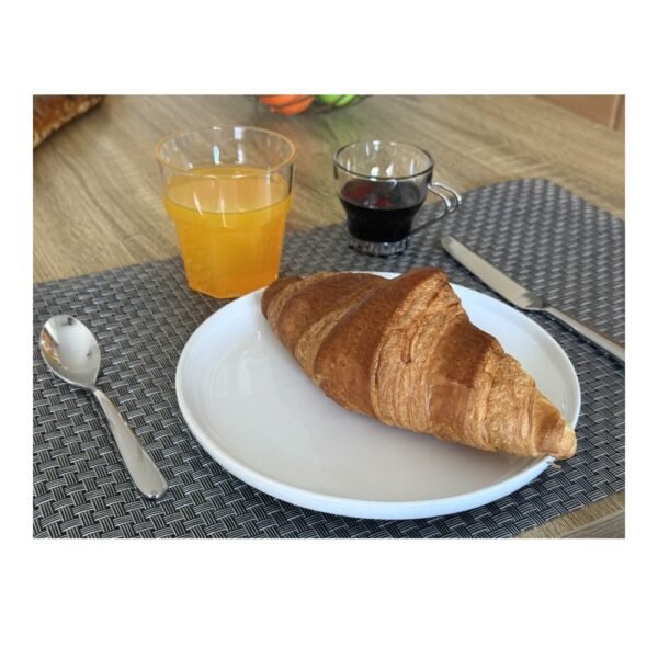 Une mise en scène de petit-déjeuner réaliste réalisée avec des factices alimentaires en résine artisanale : un croissant, un jus d'orange pressée et un café noir sur une table en bois avec un set de table gris. Créations Coq'Ci pour la photographie professionnelle et le home staging